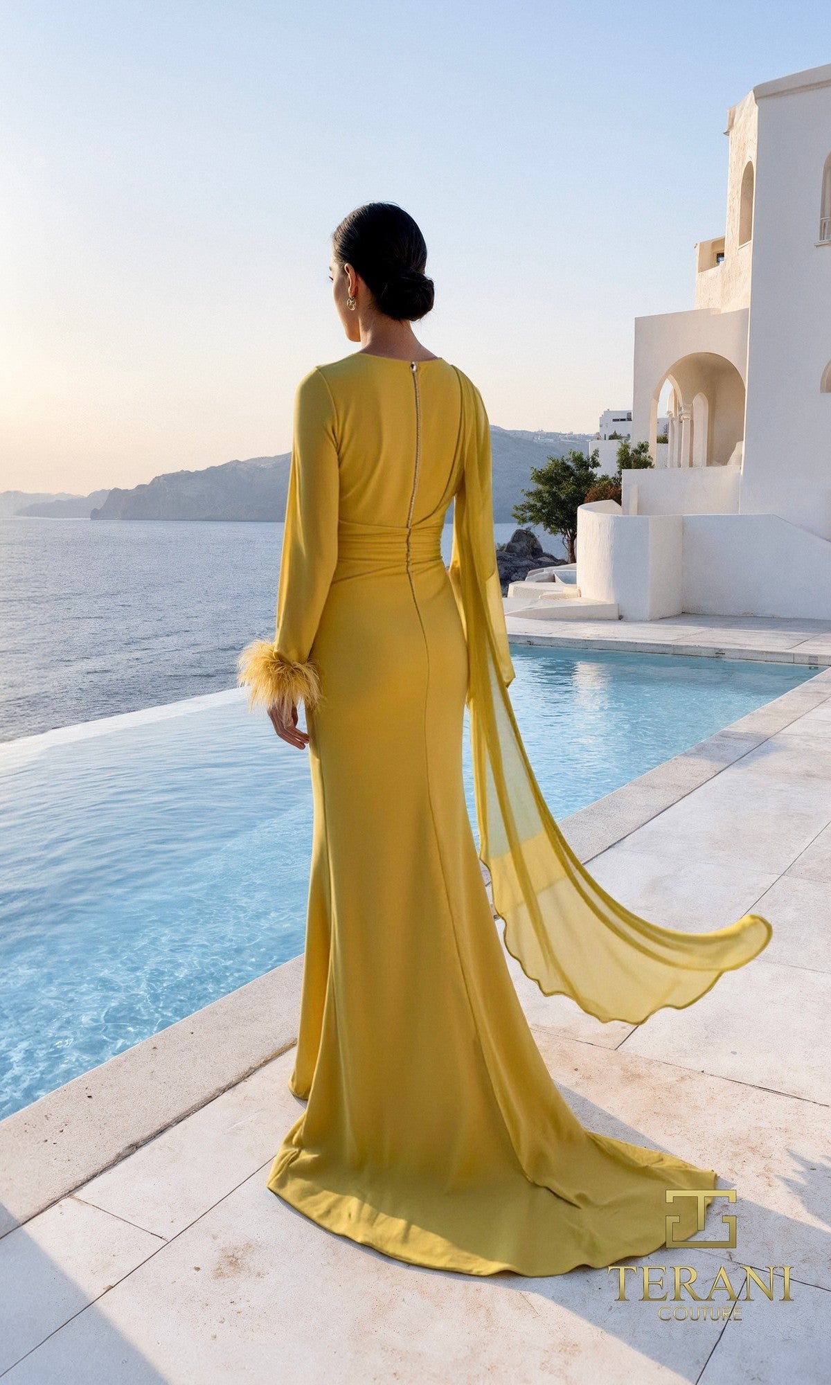 A woman in the Terani 261M6403 long formal dress with sheer sleeves and feathered cuffs stands by a pool with sea views and white buildings in the background.